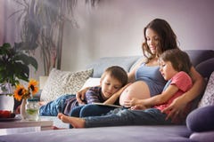 Mulher gravida nova, lendo um livro em casa a seus dois meninos fotografia de stock Mulher gravida nova, lendo um livro em casa a seus dois meninos fotografia de stock