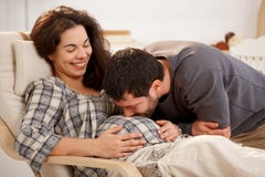 Mulher gravida que relaxa, barriga de beijo do marido fotografia de stock Mulher gravida que relaxa, barriga de beijo do marido fotografia de stock