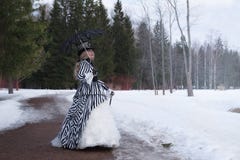 Mulher idosa em um vestido gótico em um chapéu com um guarda-chuva preto na natureza no inverno foto de stock Mulher idosa em um vestido gótico em um chapéu com um guarda-chuva preto na natureza no inverno foto de stock