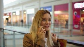 A mulher loura encantador fala no telefone que anda com os sacos de compras na alameda vídeos de arquivo A mulher loura encantador fala no telefone que anda com os sacos de compras na alameda vídeos de arquivo