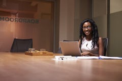 Mulher negra nova que trabalha tarde no escritório que sorri à câmera Imagem de Stock Mulher negra nova que trabalha tarde no escritório que sorri à câmera Imagem de Stock