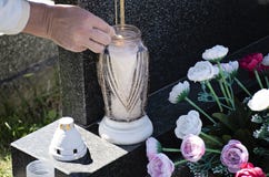A mulher no cemitério está iluminando uma vela com um fósforo na sepultura imagem de stock A mulher no cemitério está iluminando uma vela com um fósforo na sepultura imagem de stock