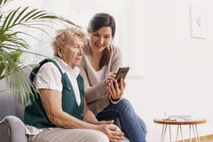 Mulher no lar de idosos com sua neta que mostra lhe como usar um telefone celular imagens de stock Mulher no lar de idosos com sua neta que mostra lhe como usar um telefone celular imagens de stock