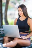 Mulher nova bonita do latino que senta em público o parque que conversa sobre o laptop imagem de stock Mulher nova bonita do latino que senta em público o parque que conversa sobre o laptop imagem de stock