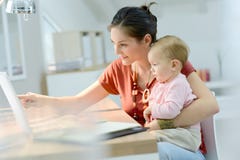 Mulher que guarda seu bebê e que trabalha no portátil foto de stock Mulher que guarda seu bebê e que trabalha no portátil foto de stock
