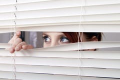 Mulher que olha através das cortinas de indicador