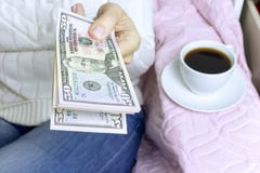 Mulher que senta-se com uma xícara de café e que guarda um bloco de cinqüênta notas de dólar imagens de stock Mulher que senta-se com uma xícara de café e que guarda um bloco de cinqüênta notas de dólar imagens de stock