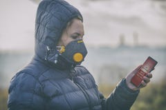 Mulher que veste uma máscara protetora contra a névoa real e que verifica a poluição do ar atual com o app esperto do telefone fotografia de stock Mulher que veste uma máscara protetora contra a névoa real e que verifica a poluição do ar atual com o app esperto do telefone fotografia de stock