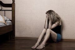 Mulher triste que senta-se apenas em uma sala vazia ao lado da cama Violência doméstica imagens de stock Mulher triste que senta-se apenas em uma sala vazia ao lado da cama Violência doméstica imagens de stock