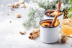 Mulled wine in white metal mugs with cinnamon, spices and orange with fir tree and christmas lights - traditional drink on winter
