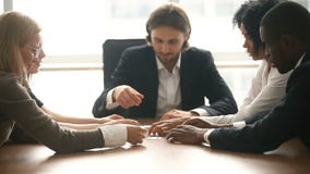 Multi-ethnic business group assembling jigsaw puzzle together at conference table