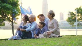 Multi generation family relaxing outdoors in park. Happy three generational family with grandparents parent and child relaxing sitting on grass in city park