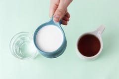 Multicolored mugs with hot drinks and female hand on a blue background, top view stock photography Multicolored mugs with hot drinks and female hand on a blue background, top view stock photography