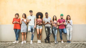 Multiracial friends using smartphone against wall at university stock photo Multiracial friends using smartphone against wall at university stock photo