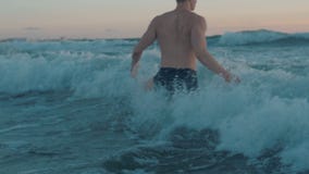 Muscular man in black underwear swimming at sunset.