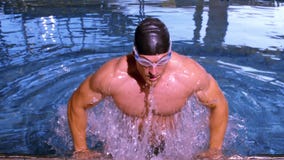Muscular swimmer emerging from pool and pulling himself up