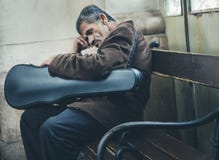 Musician sleeping on his instrument on street bench