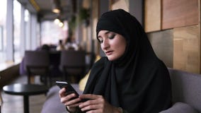 Muslim woman in cafe using her smartphone, chatting online browsing social media sharing lifestyle. Enjoying, relaxing stock video footage Muslim woman in cafe using her smartphone, chatting online browsing social media sharing lifestyle. Enjoying, relaxing stock video footage