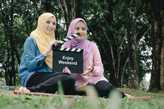 Muslimah tenant l'ardoise professionnelle de film avec le mot APPRÉCIENT LE WEEK-END, panneau de clapet de film au parc Photo stock Muslimah tenant l'ardoise professionnelle de film avec le mot APPRÉCIENT LE WEEK-END, panneau de clapet de film au parc Photo stock