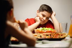 Mutter, die dem überladenen Sohn Salat anstelle der Pizza gibt stockfotografie Mutter, die dem überladenen Sohn Salat anstelle der Pizza gibt stockfotografie