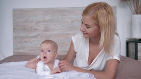 Mutter mit ihrer Tochter, die für die Kamera liegt auf Bett, Elternteil leicht aufwirft, küsst und umarmt ihr neugeborenes Mädche stock video Mutter mit ihrer Tochter, die für die Kamera liegt auf Bett, Elternteil leicht aufwirft, küsst und umarmt ihr neugeborenes Mädche stock video