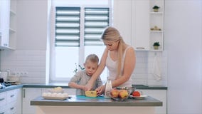Mutter unterrichtet Sohn, Käse zu hacken Eine junge schöne Mutter mit in weißem Hemd und nettem Sohnkoch in einer weißen Küche stock video Mutter unterrichtet Sohn, Käse zu hacken Eine junge schöne Mutter mit in weißem Hemd und nettem Sohnkoch in einer weißen Küche stock video