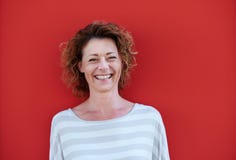 Más vieja mujer sonriente con el pelo rizado contra la pared roja Foto de archivo Más vieja mujer sonriente con el pelo rizado contra la pared roja Foto de archivo