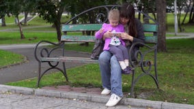 A mãe e a filha da família jogam usando um smartphone em um dia nebuloso no parque vídeos de arquivo A mãe e a filha da família jogam usando um smartphone em um dia nebuloso no parque vídeos de arquivo