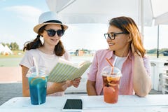 Mãe feliz e filha adolescente que falam e que sorriem Pais com uma criança em um café exterior do verão que aprecia bebidas frias imagens de stock Mãe feliz e filha adolescente que falam e que sorriem Pais com uma criança em um café exterior do verão que aprecia bebidas frias imagens de stock