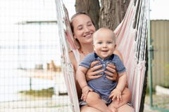Mãe nova com o bebê bonito que senta-se e que relaxa na rede perto do rio ou do lago Mamã e criança que têm o divertimento no ver imagens de stock Mãe nova com o bebê bonito que senta-se e que relaxa na rede perto do rio ou do lago Mamã e criança que têm o divertimento no ver imagens de stock