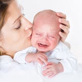 Mãe nova que beija seu bebê recém-nascido de grito Imagem de Stock Mãe nova que beija seu bebê recém-nascido de grito Imagem de Stock