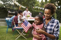 Mãe preta e bebê que guardam a bandeira no partido de jardim do 4 de julho imagens de stock Mãe preta e bebê que guardam a bandeira no partido de jardim do 4 de julho imagens de stock