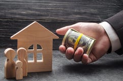 A mão de um homem de negócios estende o dinheiro a uma casa de madeira A família está estando perto da casa O conceito da compra foto de stock royalty free A mão de um homem de negócios estende o dinheiro a uma casa de madeira A família está estando perto da casa O conceito da compra foto de stock royalty free