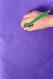 A mão de um rapaz pequeno pinta um lápis verde em um papel roxo imagem de stock A mão de um rapaz pequeno pinta um lápis verde em um papel roxo imagem de stock