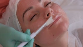 A mão do cosmetologist aplica o gel à cara fêmea com uma escova branca Menina bonita no sal?o de beleza Close-up pele video estoque A mão do cosmetologist aplica o gel à cara fêmea com uma escova branca Menina bonita no sal?o de beleza Close-up pele video estoque