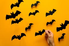 Mão do ` s da mulher que mantém o bastão e os bastões pretos do papel que voam no fundo amarelo Conceito de Halloween fotografia de stock royalty free Mão do ` s da mulher que mantém o bastão e os bastões pretos do papel que voam no fundo amarelo Conceito de Halloween fotografia de stock royalty free