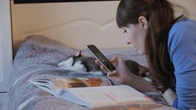 Mädchen auf dem Bett mit dem Telefon, der Welpe des sibirischen Huskys, der neben ihr schläft stock video Mädchen auf dem Bett mit dem Telefon, der Welpe des sibirischen Huskys, der neben ihr schläft stock video