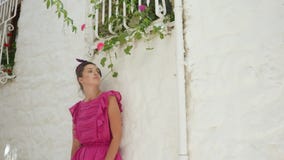 Mädchen in der rosa kurzen Kleiderstellung an der weißen Steinwand an einem Sommertag stock footage Mädchen in der rosa kurzen Kleiderstellung an der weißen Steinwand an einem Sommertag stock footage
