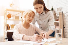 Mädchen pflegt ältere Frau zu Hause Mädchen hilft Frau schreiben lizenzfreies stockfoto Mädchen pflegt ältere Frau zu Hause Mädchen hilft Frau schreiben lizenzfreies stockfoto
