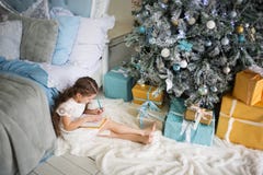 Mädchen schreibt Santa Claus einen Brief im Raum mit Bett und im Weihnachtsbaum in den Blau- und Goldfarben lizenzfreie stockbilder Mädchen schreibt Santa Claus einen Brief im Raum mit Bett und im Weihnachtsbaum in den Blau- und Goldfarben lizenzfreie stockbilder