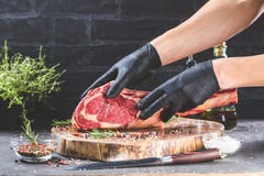 Männliche Hände des Metzger- oder Kochholdingkriegsbeil-Rindfleischsteaks auf dunklem rustikalem Küchentischhintergrund stockbilder Männliche Hände des Metzger- oder Kochholdingkriegsbeil-Rindfleischsteaks auf dunklem rustikalem Küchentischhintergrund stockbilder