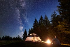 Männliche Wanderer enjoyng Nacht, die nahe touristischem Zelt am Lagerfeuer unter blauem sternenklarem Himmel und Milchstraße kam stockbild Männliche Wanderer enjoyng Nacht, die nahe touristischem Zelt am Lagerfeuer unter blauem sternenklarem Himmel und Milchstraße kam stockbild