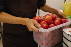 Männlicher Koch in einem braunen Schutzblech in der Küche mit einem Korb von roten Tomaten in seinen Händen Der Prozess des Koche stockfotografie Männlicher Koch in einem braunen Schutzblech in der Küche mit einem Korb von roten Tomaten in seinen Händen Der Prozess des Koche stockfotografie