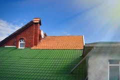 Mångfärgade belade med tegel tak av hus mot den blåa himlen med molnbakgrundslofter apelsin och solstrålar för grön färg arkivfoton Mångfärgade belade med tegel tak av hus mot den blåa himlen med molnbakgrundslofter apelsin och solstrålar för grön färg arkivfoton