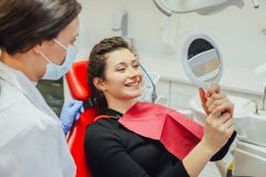 Młoda kobieta sprawdza ich zęby przy lustrem po stomatologicznego traktowania - Zaludnia bodycare i stomatology pojęcie dla zdrow fotografia stock Młoda kobieta sprawdza ich zęby przy lustrem po stomatologicznego traktowania - Zaludnia bodycare i stomatology pojęcie dla zdrow fotografia stock