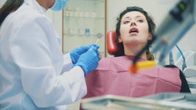 Młodej kobiety obsiadanie na dentysty krześle przy lekarki przyjęciem Poważny pacjent otwiera jego usta zbiory Młodej kobiety obsiadanie na dentysty krześle przy lekarki przyjęciem Poważny pacjent otwiera jego usta zbiory