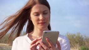 Móbil do uso da mulher contra o céu azul Conversa fêmea de sorriso com os amigos através do telefone celular no movimento lento filme Móbil do uso da mulher contra o céu azul Conversa fêmea de sorriso com os amigos através do telefone celular no movimento lento filme