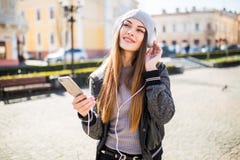 Música que escucha de la mujer en línea con los auriculares inalámbricos de un smartphone en la calle en un día soleado del veran Foto de archivo Música que escucha de la mujer en línea con los auriculares inalámbricos de un smartphone en la calle en un día soleado del veran Foto de archivo