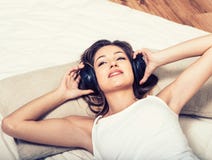 Música que escucha de los auriculares hermosos jovenes de la mujer en cama fotografía de archivo Música que escucha de los auriculares hermosos jovenes de la mujer en cama fotografía de archivo