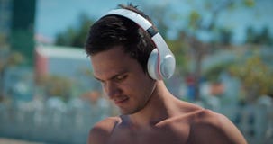 Música que escucha hermosa del hombre joven de su Smartphone en los auriculares blancos inalámbricos, bailando en la playa urbana metrajes Música que escucha hermosa del hombre joven de su Smartphone en los auriculares blancos inalámbricos, bailando en la playa urbana metrajes